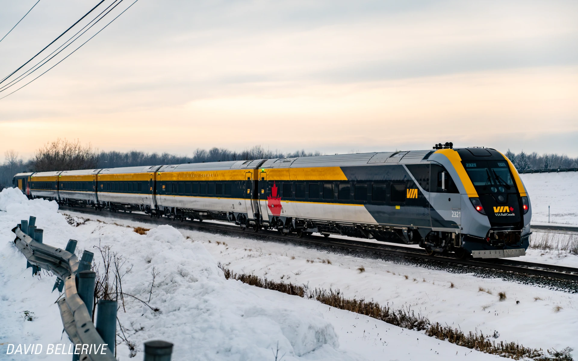 A VIA Rail passenger train traveling through a snowy rural landscape in winter.